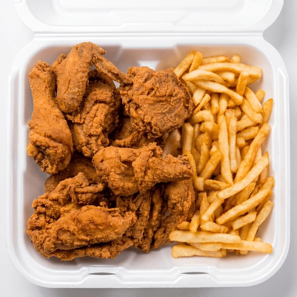 Crispy fried chicken pieces and golden french fries in a white takeout container.