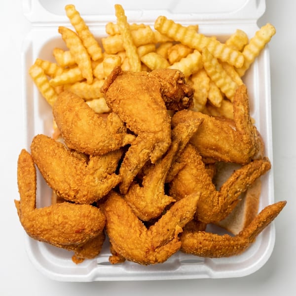 Crispy fried chicken wings and crinkle-cut fries in a white takeout container.