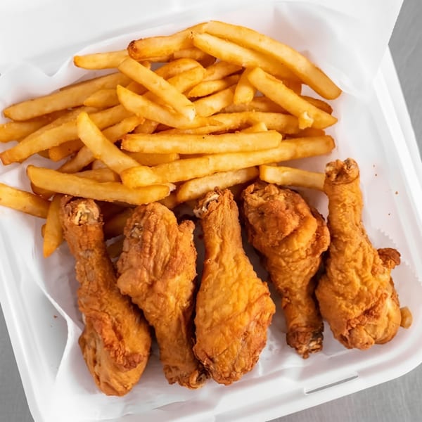 Golden-brown fried chicken drumsticks and crispy french fries in a white takeout container.