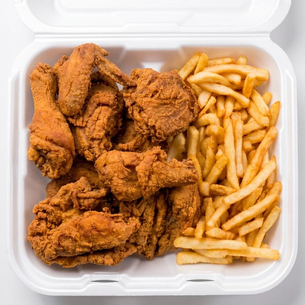 Fried chicken pieces and french fries in a white styrofoam takeout container.