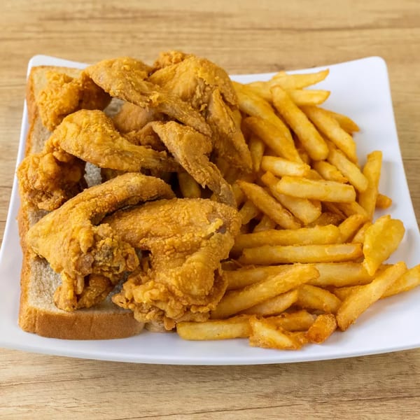 Crispy fried chicken pieces and golden french fries served on a white plate with a slice of bread.