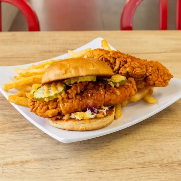 Spicy fried chicken sandwich with pickles and coleslaw, served with fries and a chicken tender.