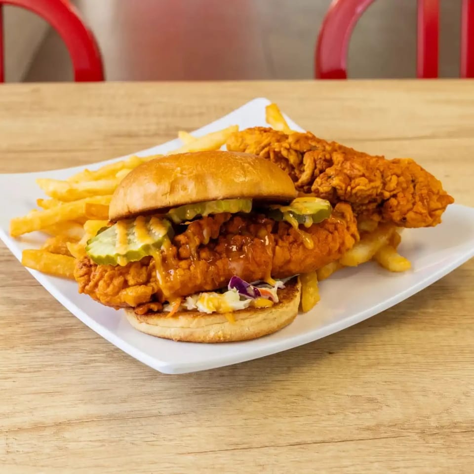 Spicy fried chicken sandwich with pickles and coleslaw, served with fries and a chicken tender.